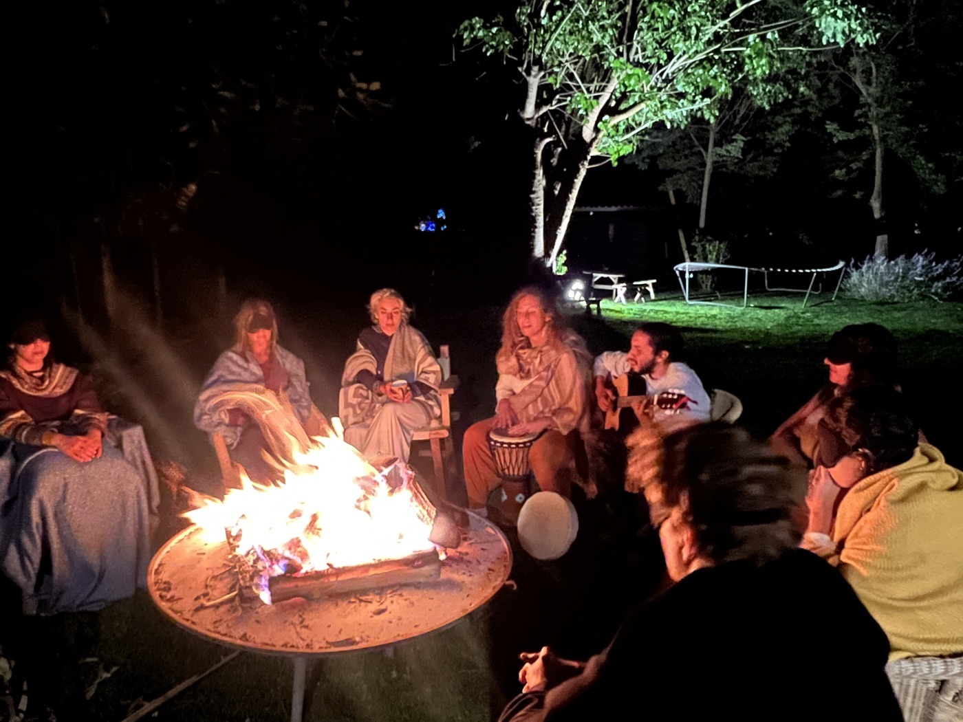 Participants gathered around a fire in the garden at night